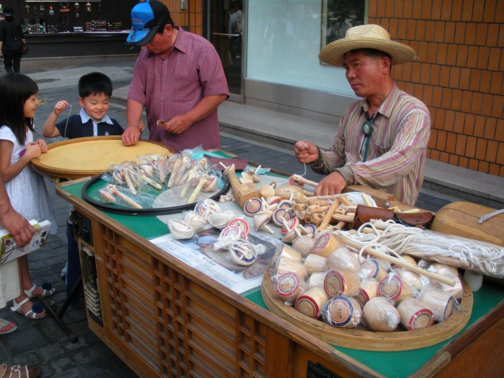 Street vendors on Insa-Dong street in Seoul, South Korea show children how to spin traditional spinning tops and wooden toys. (Seth Lewis)