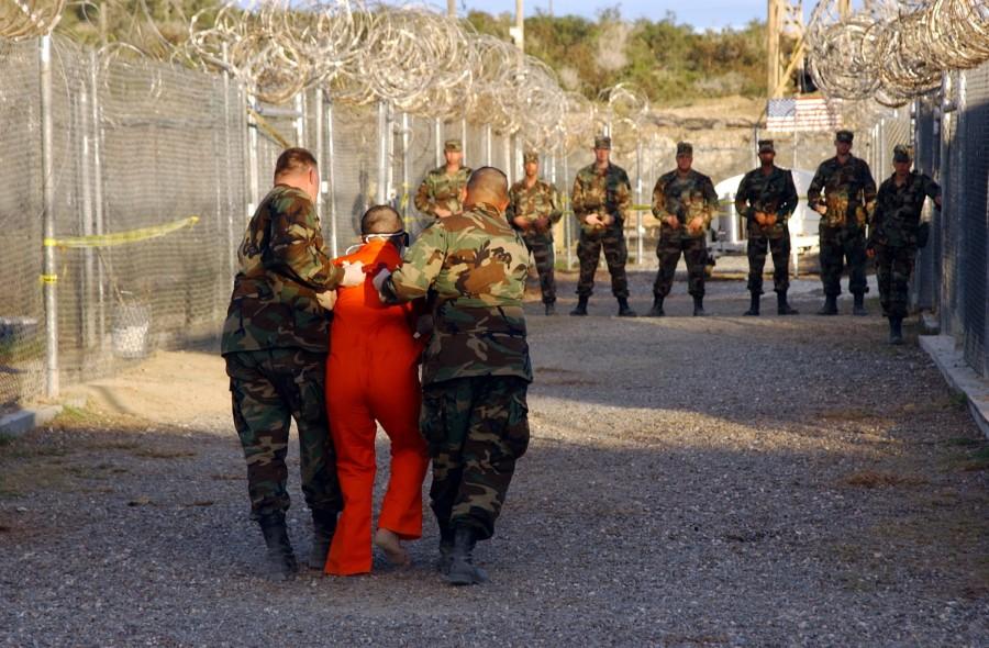 Taliban+and+al-Qaida+detainees+in+orange+jumpsuits+sit+in+a+holding+area+during+in-processing+to+the+temporary+detention+facility+on+Jan.+18%2C+2002%2C+in+Guantanamo+Bay%2C+Cuba.+Photo+from+MCT+Campus