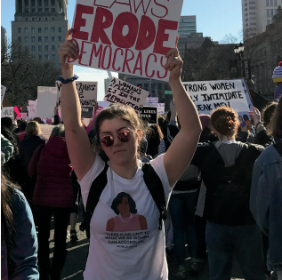 Photo of Oyster at the St. Louis Womens March holding a sign reading, Voter suppression laws erode democracy. 