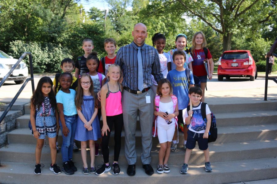 Patrick Fisher stands outside school smiling with some of his students