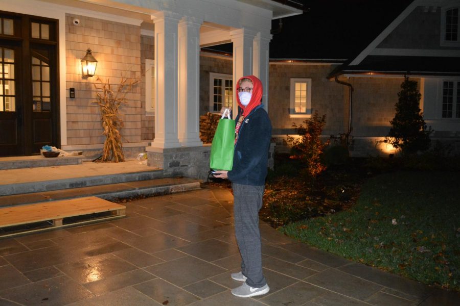 A young masked man walks up to a house to deliver a bag of food purchased through the subdivision delivery program. 