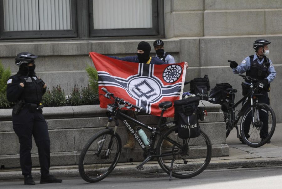 A man with a ski mask is surrounded by police officers at a reopen Illinois rally outside Chicago's Thompson Center, May 16, 2020. As the rally was winding down, he walked around with a banner with an apparent Neo-Nazi sign.