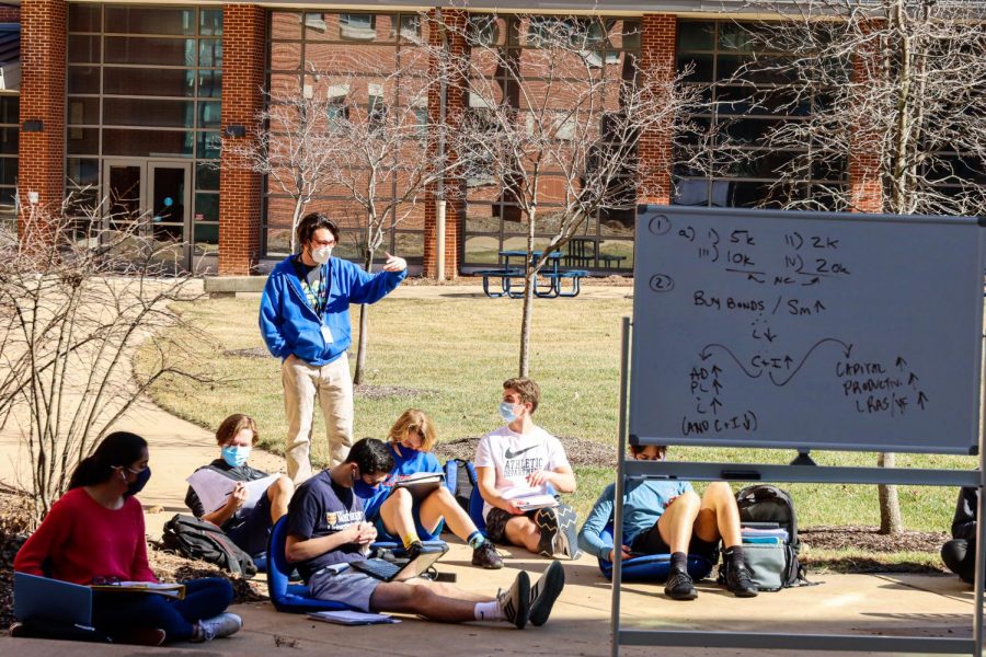 Economics teacher Daniel Glossenger is giving a lecture to a few of his students in the CHS quad on a sunny, warm day.  