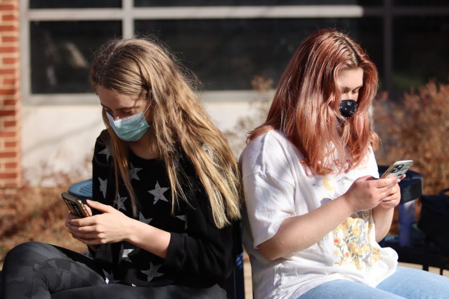 Masked CHS students sit outside in the quad, engrossed in their phones. 