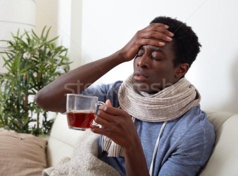 A Black man, holding his head in pain and drinking a cup of tea.