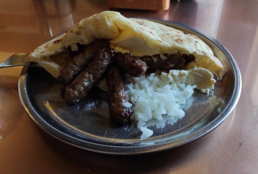 A plate of cevapi, a dish of grilled minced meat. Here, its served with flatbread called somun, onions, and a clotted cream called kajmak. 