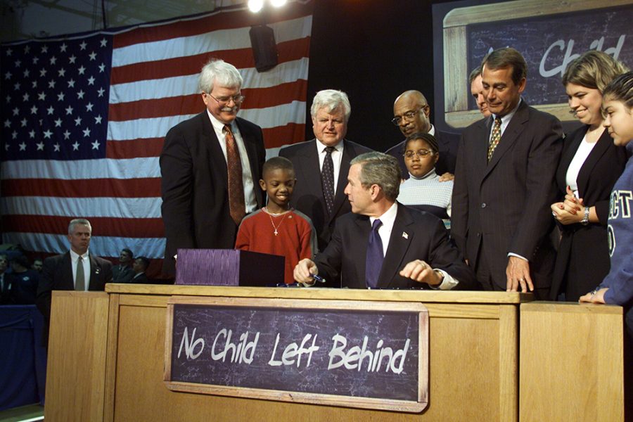 President George W. Bush signs the No Child Left Behind Act into law at a high school in Hamilton, OH, 2002. Bush is flanked by congressmen, cabinet members, and students. 