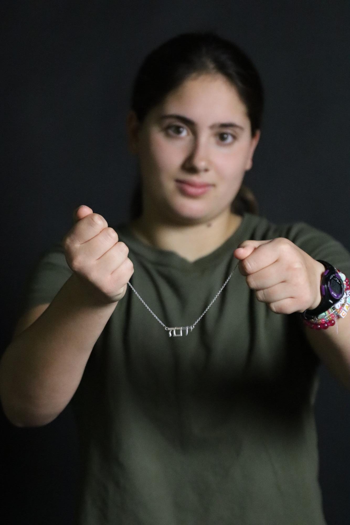 Alex Cohen holds a silver necklace with her Hebrew name, הנוי. The necklace was a gift from family friends for her bat mitzvah She wears the necklace every day. 