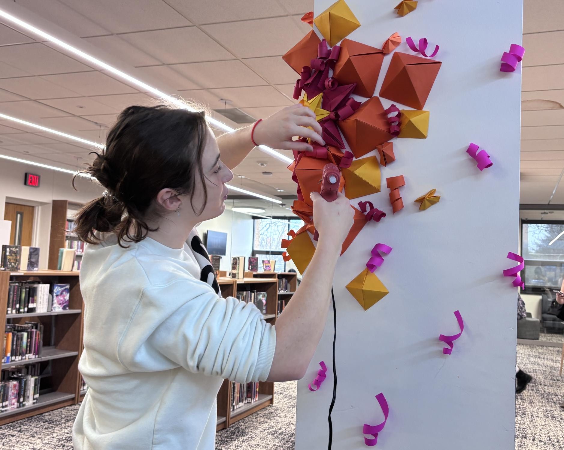 Senior Noa BenShahar puts the finishing touches on her project. This portion of the installation can be found in the library.  “The most memorable experience was working together and figuring out how each person was going to contribute to the overall composition,” BenShahar said. “The repetition of cutting and folding the origami was also very satisfying."