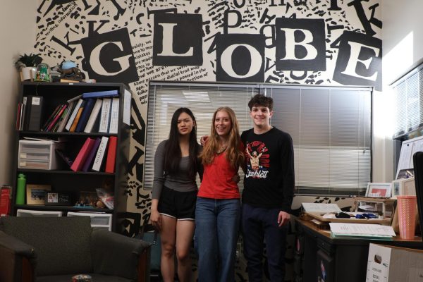 Seniors Bethany Lai, Charlie Meyers and Micah Lotsoff stand together in front of a journalism mural for their last Globe issue together.