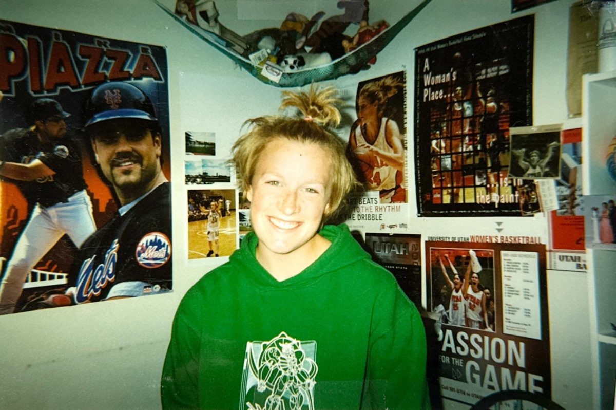 Standing in her childhood bedroom, PE/Health Teacher Sarah Gietschier-Hartman poses in front of signs of her role models. Gietschier-Hartman was inspired by these people's ambition. ”The athletes and quotes on these walls inspired me then, and the person standing here is still fueled by the same ambition,” Gietschier-Hartman said. (Photo Courtesy of Sarah Gietschier-Hartman)